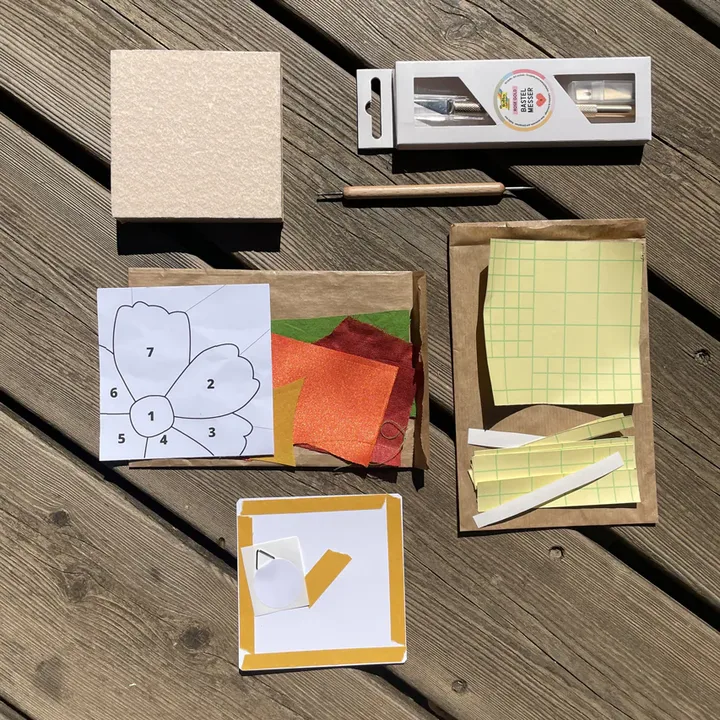 Le contenu du kit découverte posé à plat : support, adhésifs, gabarit, outils, fond de cadre et chutes de tissus